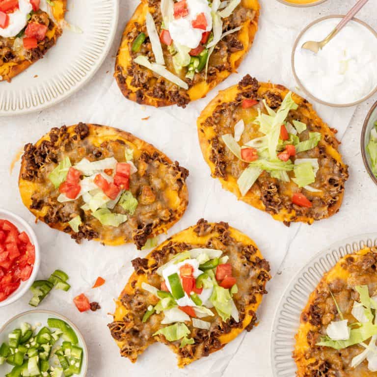 Taco pizzas on a table with toppings.