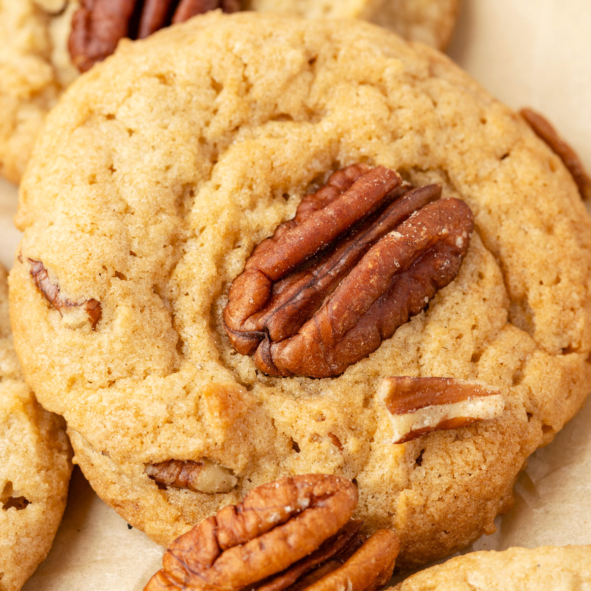 Butter pecan cookies, stacked up against each other on a piece of parchment paper with extra pecans on the table.