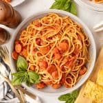 Spaghetti and hotdog in a bowl with fresh basil and garlic bread