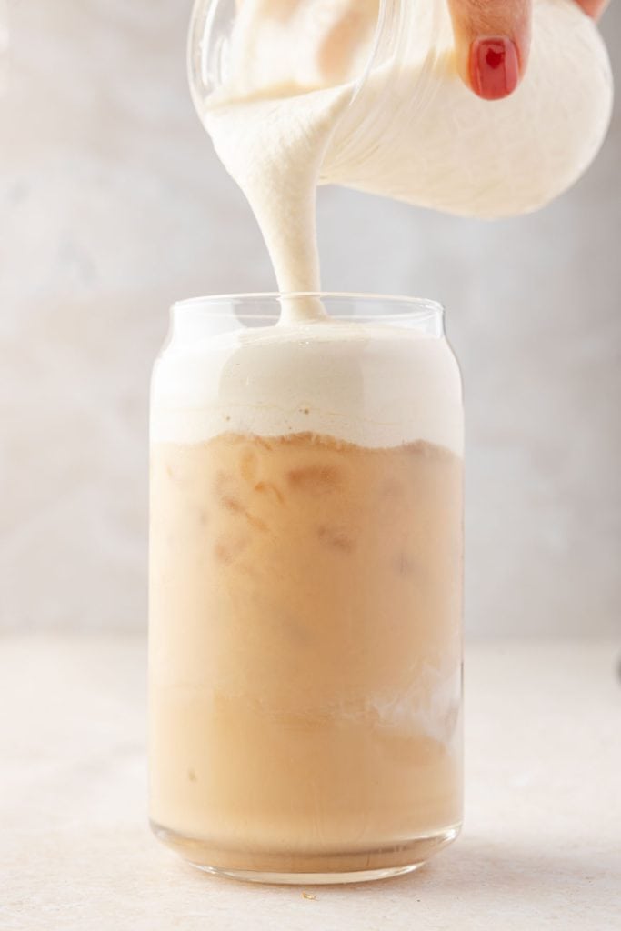 Pouring cold foam over gingerbread chai latte