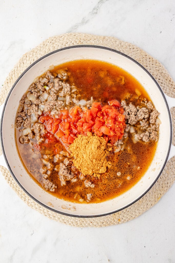 Ground beef, beef, broth, rotelle, and taco seasoning in a skillet