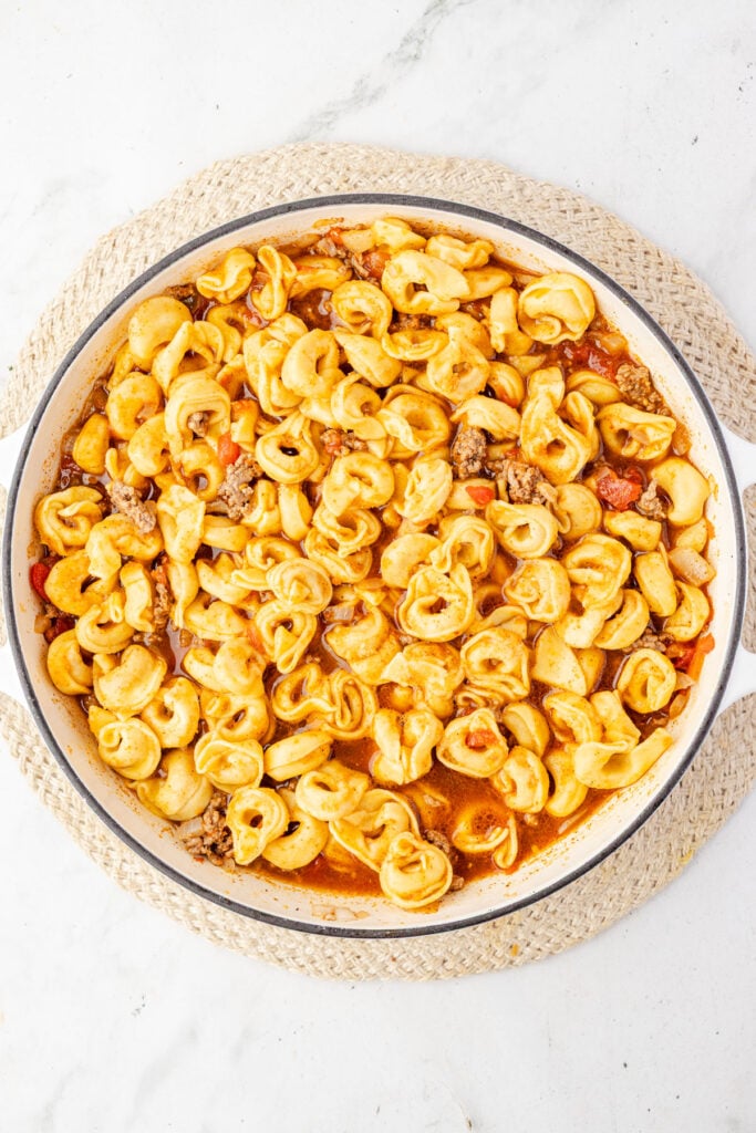 Uncooked tortellini in the taco sauce in a skillet.