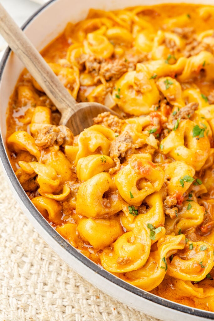 One Pot Taco TortelliniWeb023 Up close image of taco tortellini with a wooden spoon inside of a skillet.