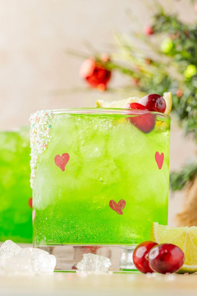 Grinch margarita and a glass with hearts and a small Christmas tree in the background