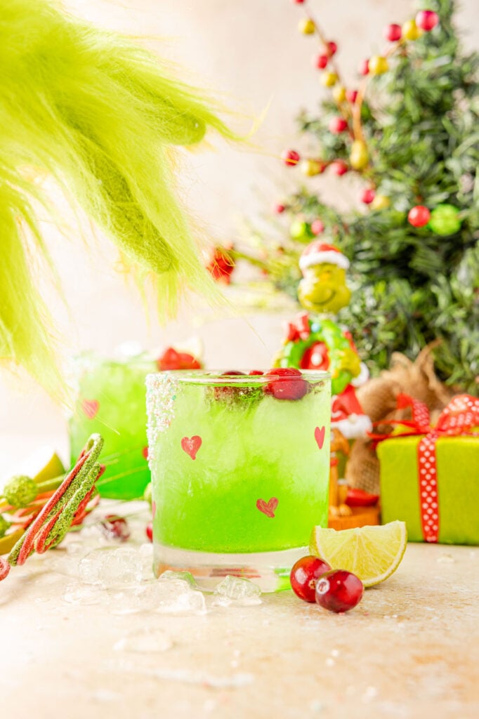 Grinch margarita on a Christmas scene with a grinch hand coming to grab the grinch cocktail