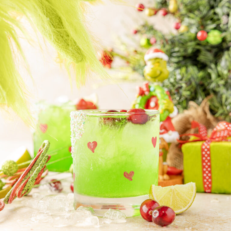 Grinch Margarita on a Christmas scene with a grinch hand coming to pick up the drink