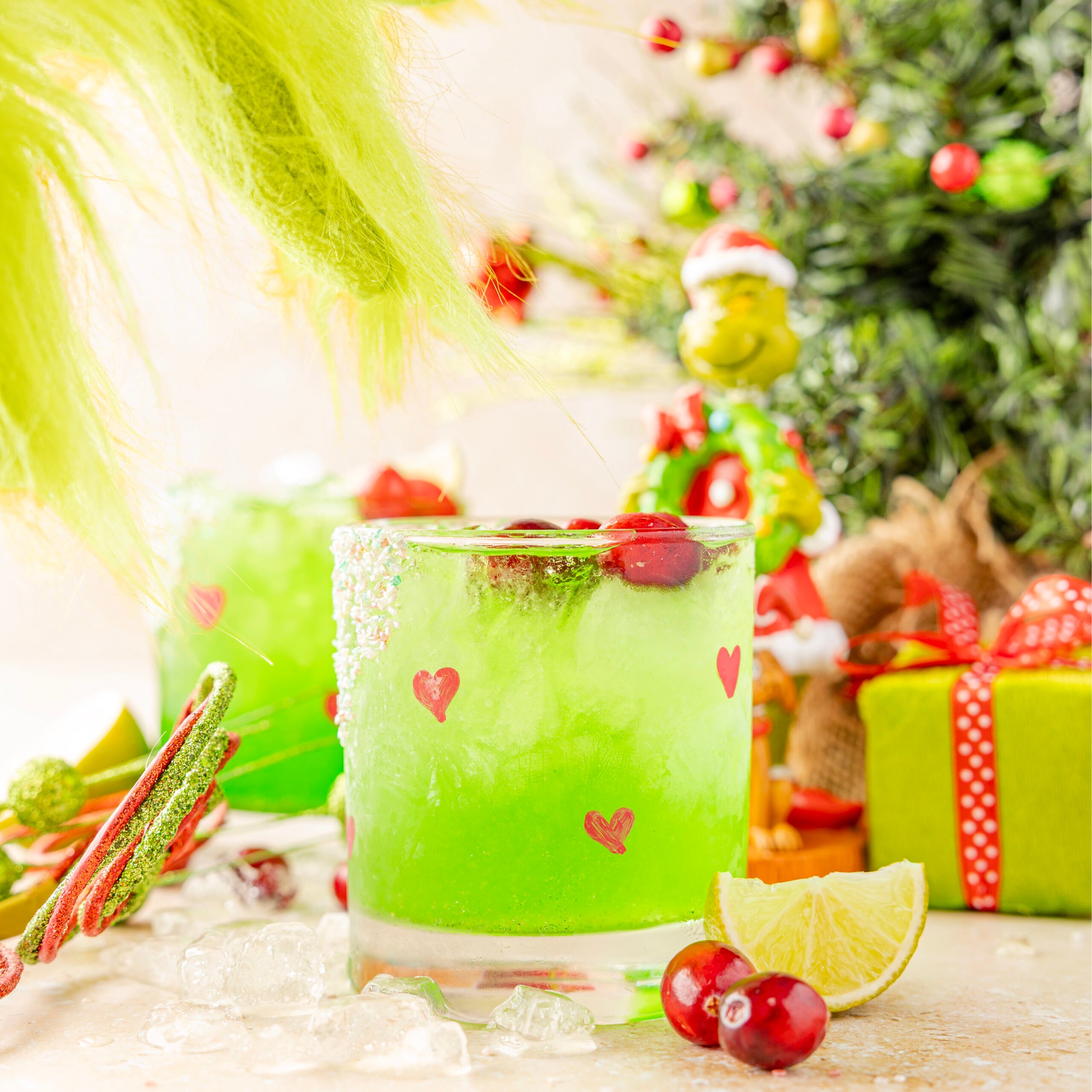 Grinch Margarita on a Christmas scene with a grinch hand coming to pick up the drink
