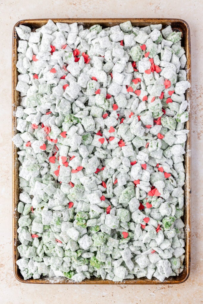 Grinch Puppy Chow on a sheet pan with heart sprinkles on top.