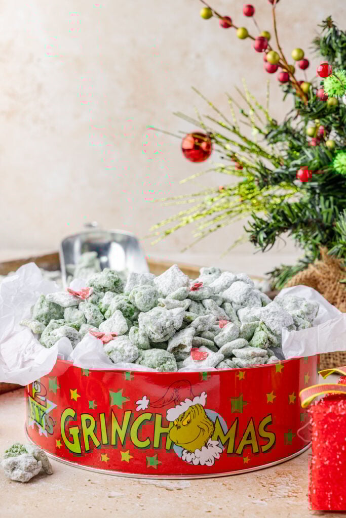 Grinch Puppy Chow in a grinch tin with a christmas tree in the background.