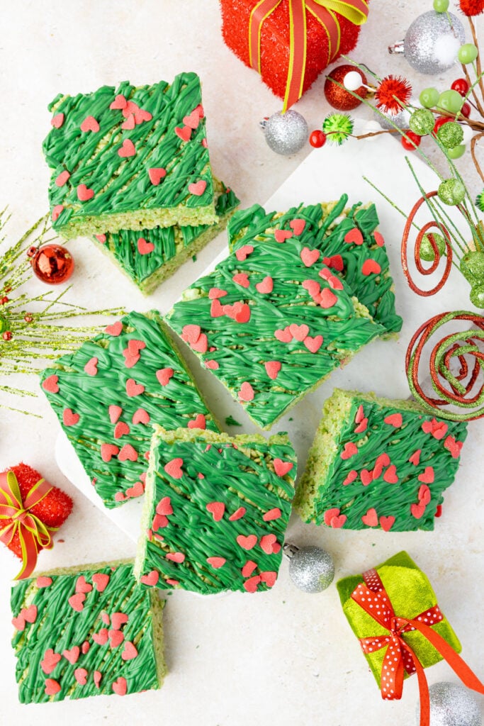 Cut grinch rice crispy treats on a styling board with lots of grinch decorations around them