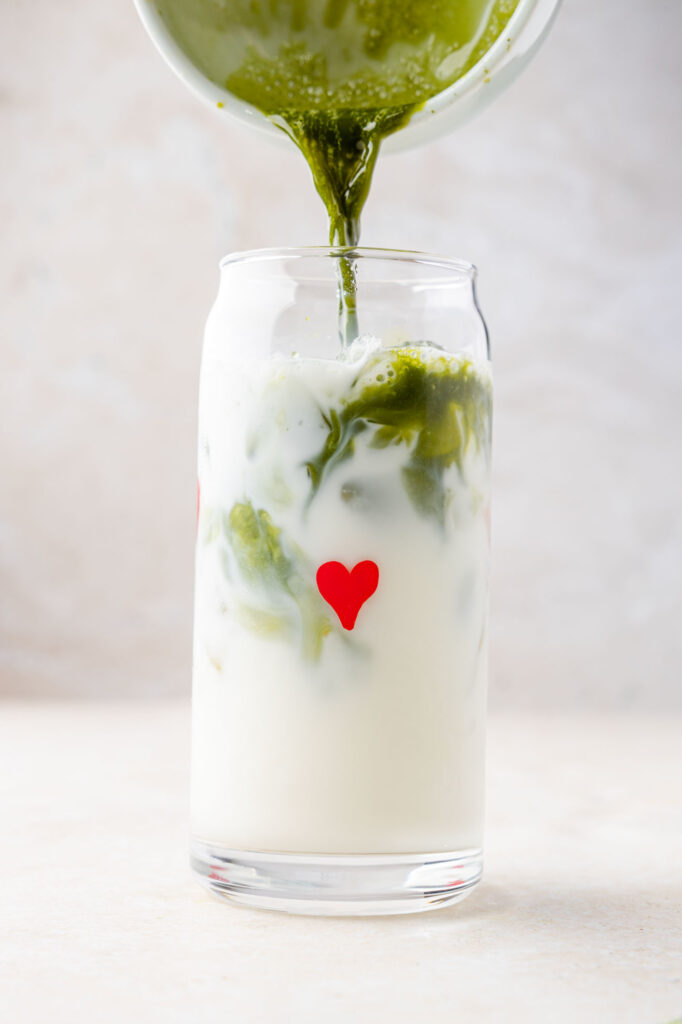 Matcha being poured into cup of milk with hearts on it