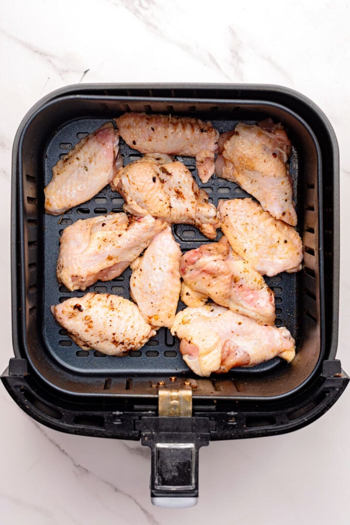 Seasoned chicken wings in an air fryer basket.