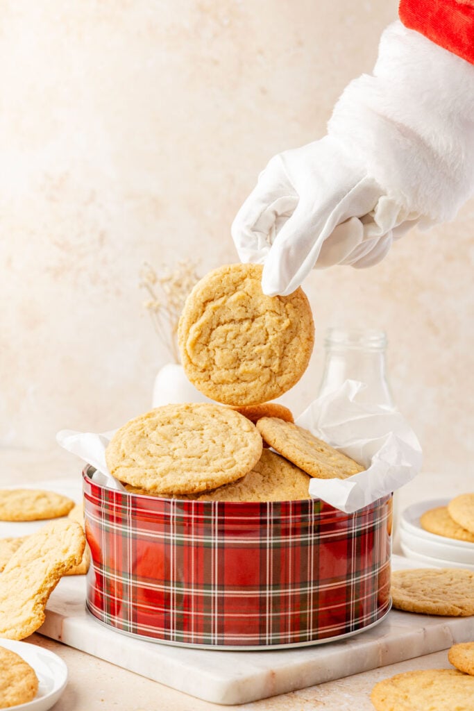Santas hand coming into steal a cookie from a tin of chocolate chips cookies