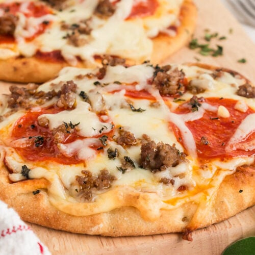 naan flatbread pizza on a cutting board with fresh herbs.