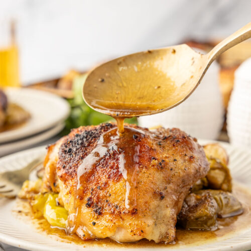 Pouring the sauce from the pan over the baked chicken thigh.