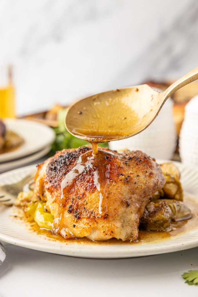 Pouring the sauce from the pan over the baked chicken thigh.
