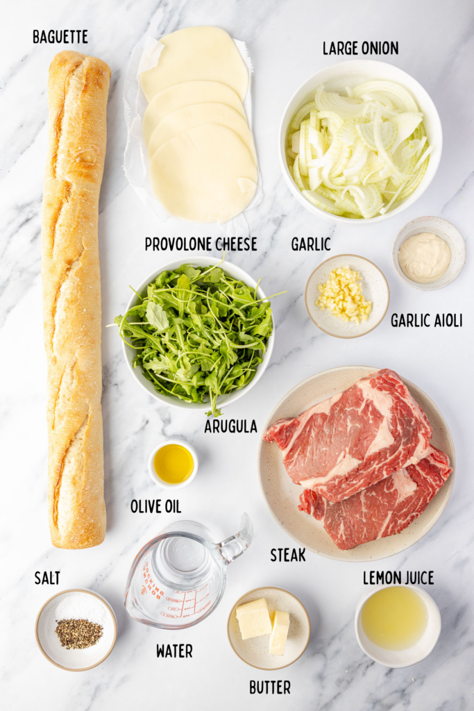 Ingredients for ribeye steak sandwich on a marble board and individual bowls