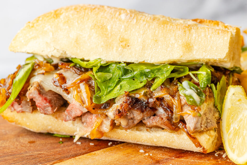 Steak sandwich on a cutting board with a lemon wedge