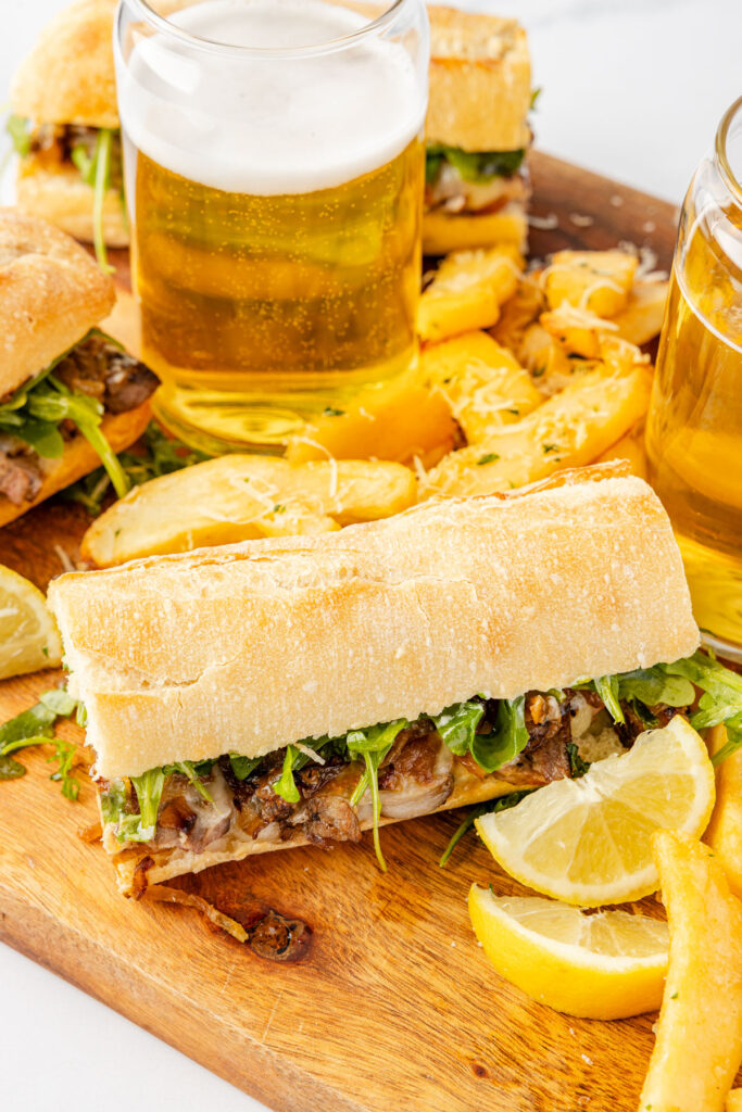 Steak Sandwich on a cutting board with french fries and beer