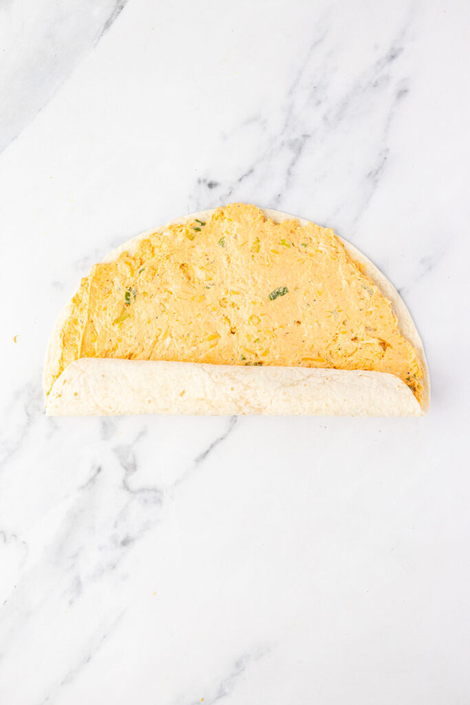 Rolling the tortilla up that is filled with buffalo chicken fill