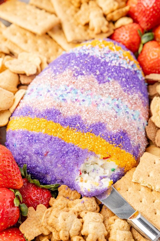 Easter cheese ball surrounded by different crackers and strawberries with a knife scooping out some of the filling