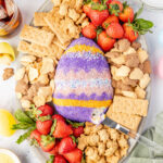 Easter cheesecake ball on a platter with crackers and fruit with a knife scooping out the inside