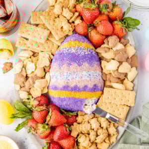 Easter cheesecake ball on a platter with crackers and fruit with a knife scooping out the inside