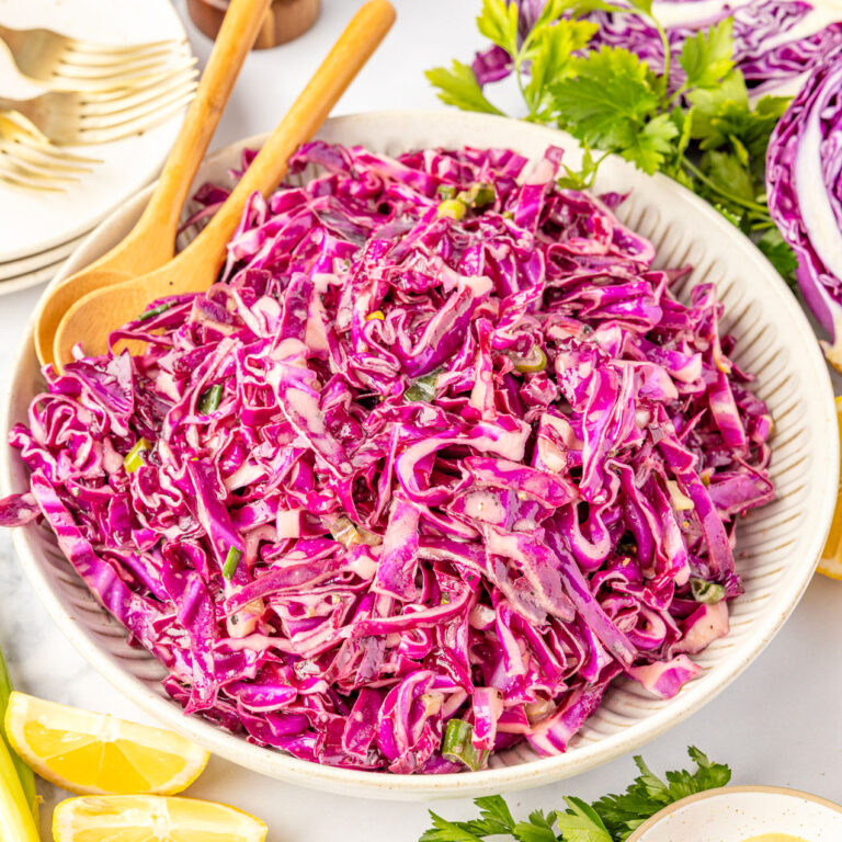 Red Cabbage Slaw in a bowl with spoons topped with green onions
