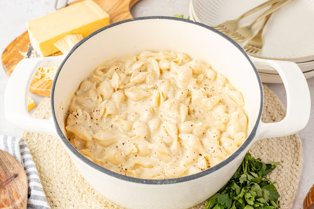 Smoked Gouda Mac and Cheese in a Dutch oven with cheese and herbs and plates around it