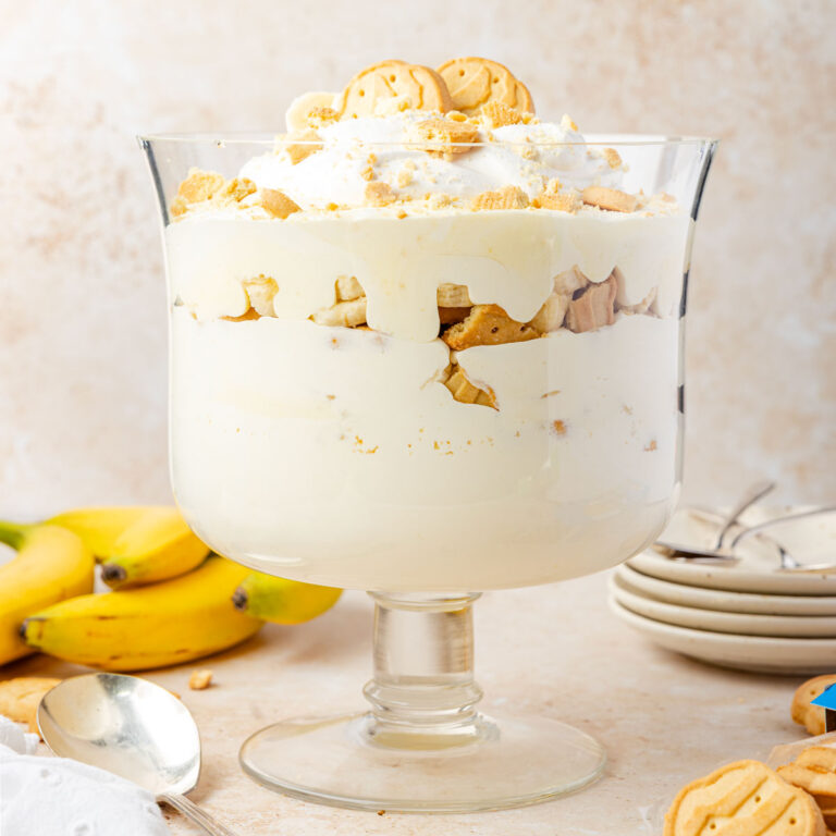 Trefoil Banana Pudding in a trifle dish with plates and bananas and Girl Scout cookies surrounding it