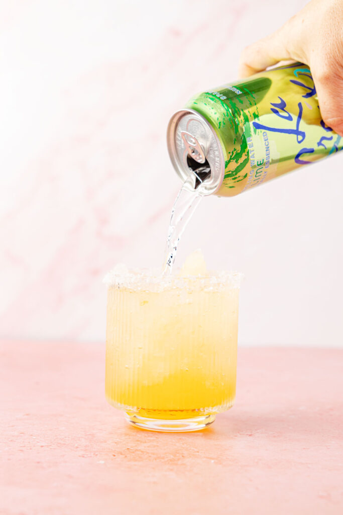pouring sparkling water in a glass with the margarite mix