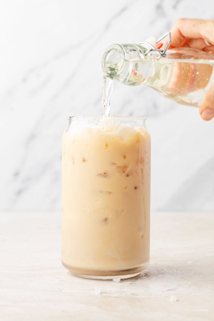 Iced chai latte in a cup pouring simple syrup into it