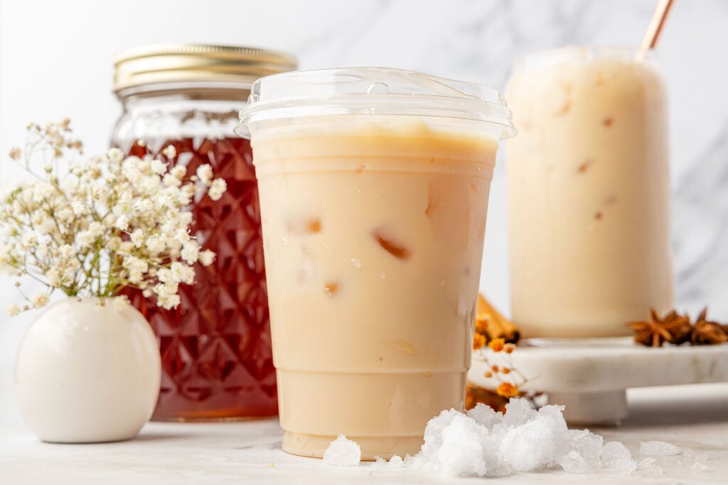 Iced chai latte in a Togo cup with iced chai latte concentrate in another chai latte in the background