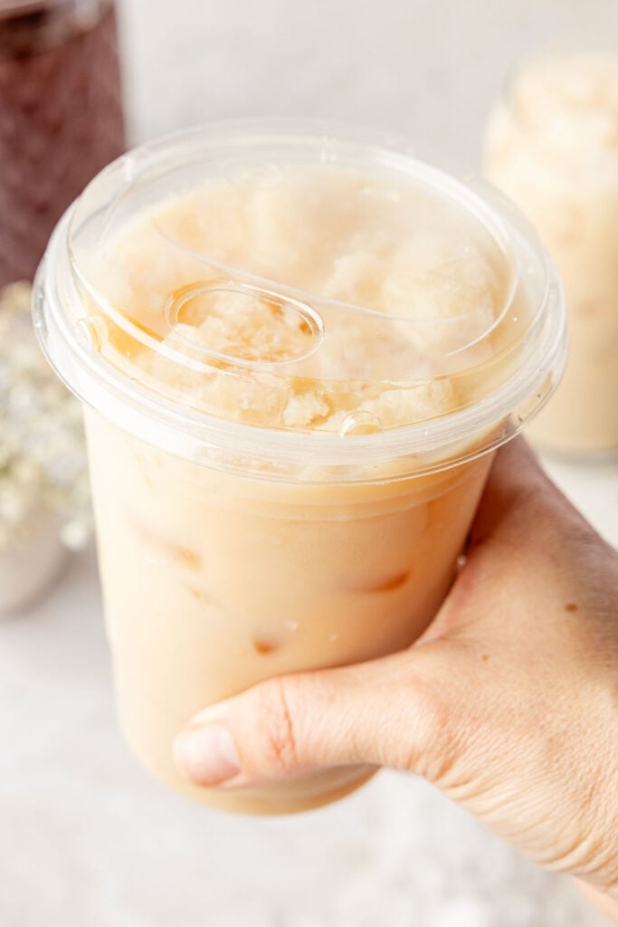 Iced chai latte in a cup to go with a hand holding it