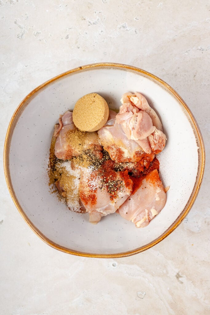 Chicken thighs in a mixing bowl with spices and brown sugar