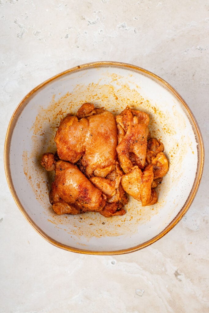 Seasoned chicken thighs in a mixing bowl