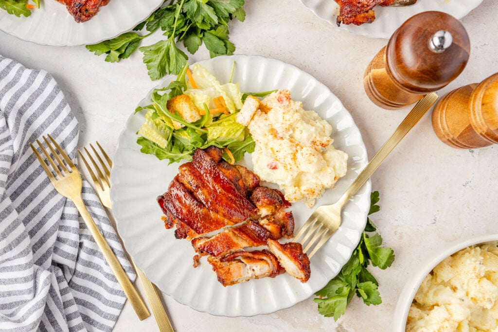 Bacon Wrapped Chicken Thighs cut on a plate with poatoes and vegeatables