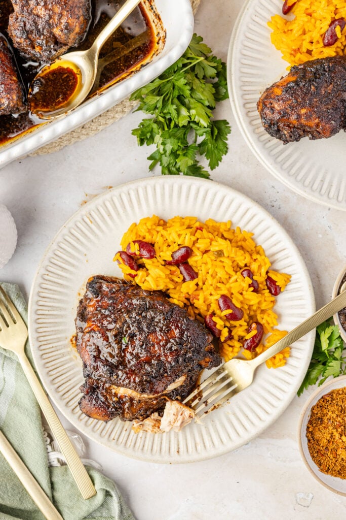 Close-up of baked jerk chicken in a casserole pan and jerk chicken on a plate with beans and rice