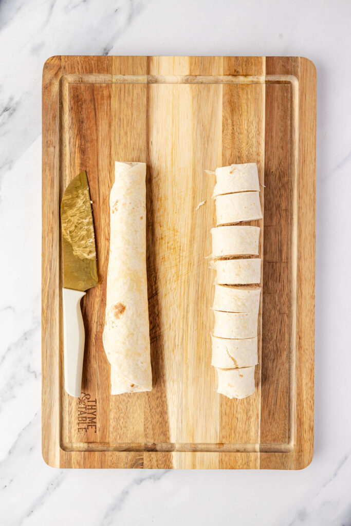 Cutting individual cracked chicken filled pinwheels on a cutting board