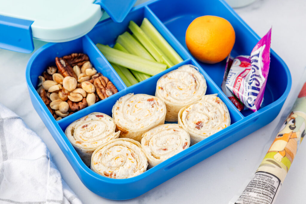 Crack, chicken, pinwheels in a lunchbox with nuts, celery, orange, fruit snacks