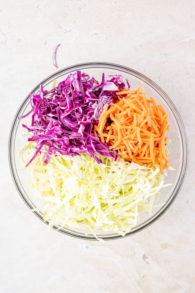 Green cabbage, red, cabbage, carrots in a large mixing bowl