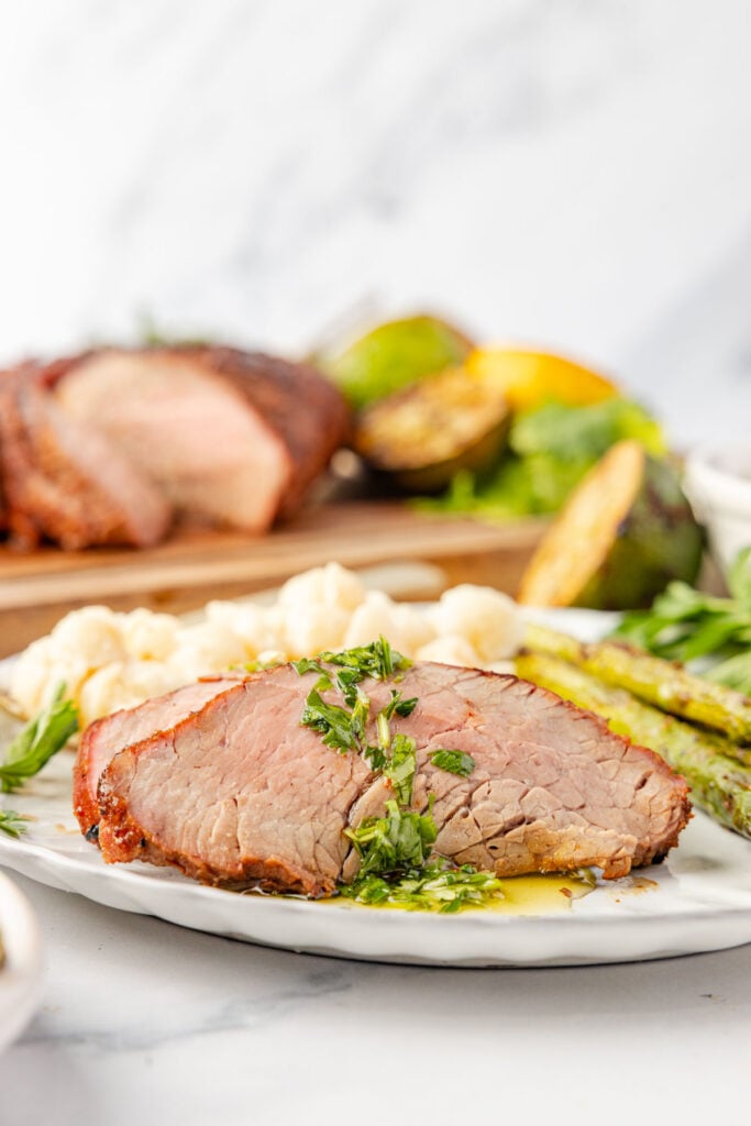 Grilled Tri Tip sliced on a plate with chimichurri sauce and mac & cheese, cheese and asparagus