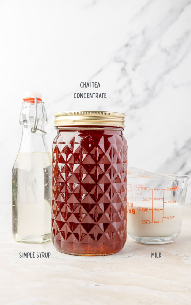 He mason jar of ice, chai latte concentrate, a jar of simple syrup, and a measuring cup of milk