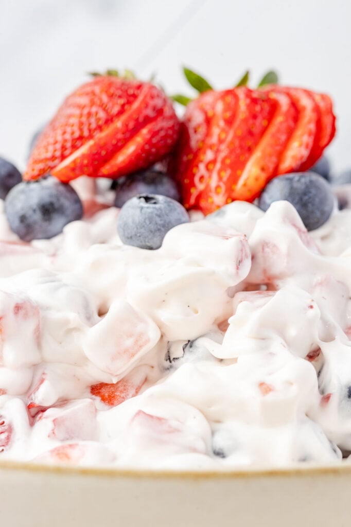 Up close Red White & Blue Cheesecake Salad in a bowl top of blueberries and strawberries