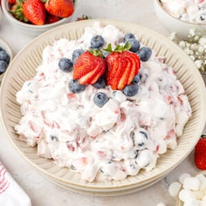 Red White & Blue Cheesecake Salad in a bowl, tap with strawberries and blueberries