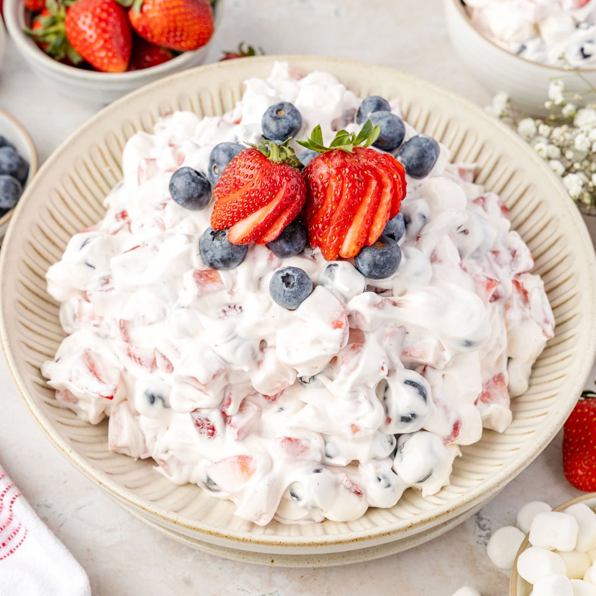 Red White & Blue Cheesecake Salad in a bowl, tap with strawberries and blueberries
