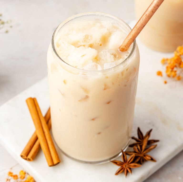 Iced Chai Latte in a glass cup with a straw with spices around it on a marble board