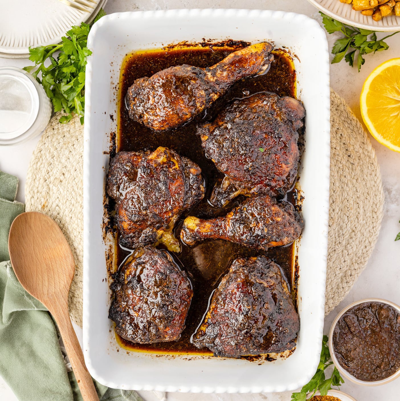 Baked Jerk Chicken in a casserole pan with a bowl of jerk paste and spices around it in a wooden spoon