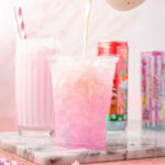 Heavy cream being poured into a cup of Alani on a pink background with a marble slab