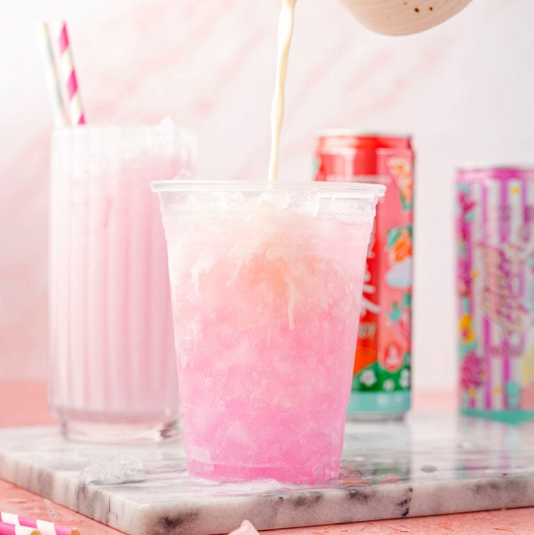 Heavy cream being poured into a cup of Alani on a pink background with a marble slab